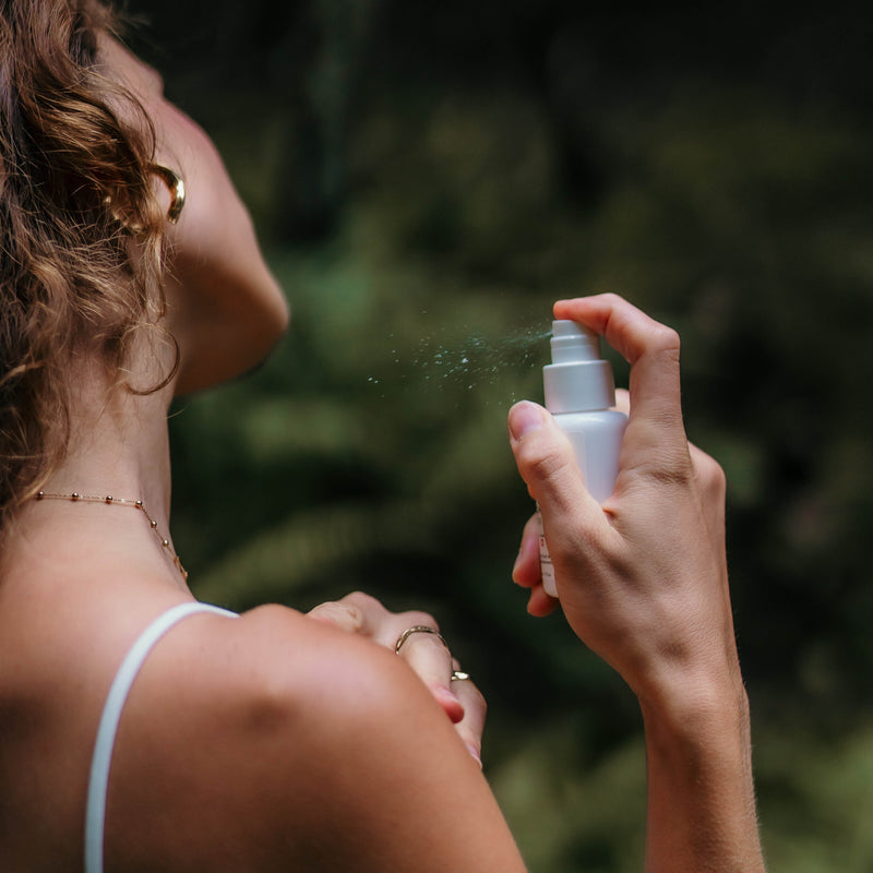 
Femme vaporisant un spray sur sa peau dans un cadre naturel, évoquant une sensation de bien-être et de fraîcheur en harmonie avec la nature.